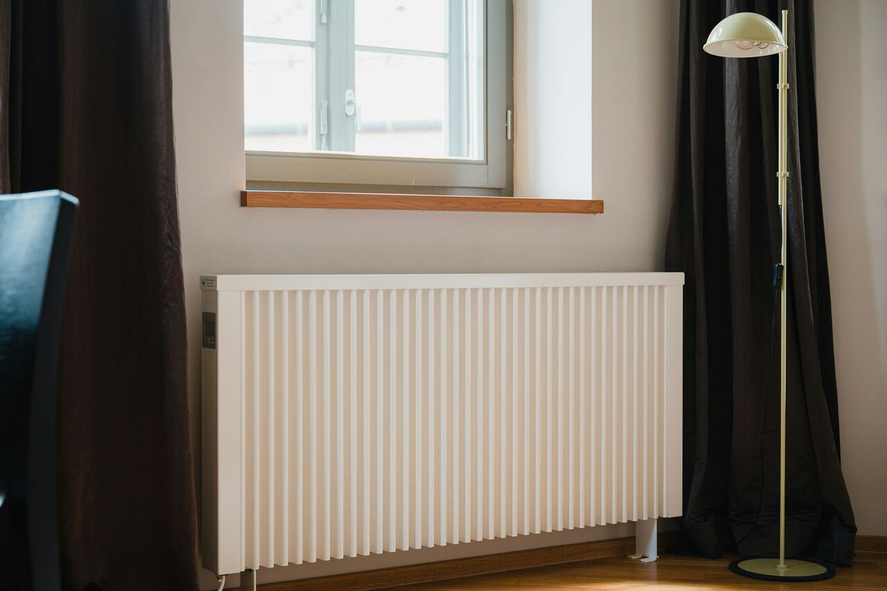 Radiateur blanc sous une fenêtre, dans une pièce lumineuse.