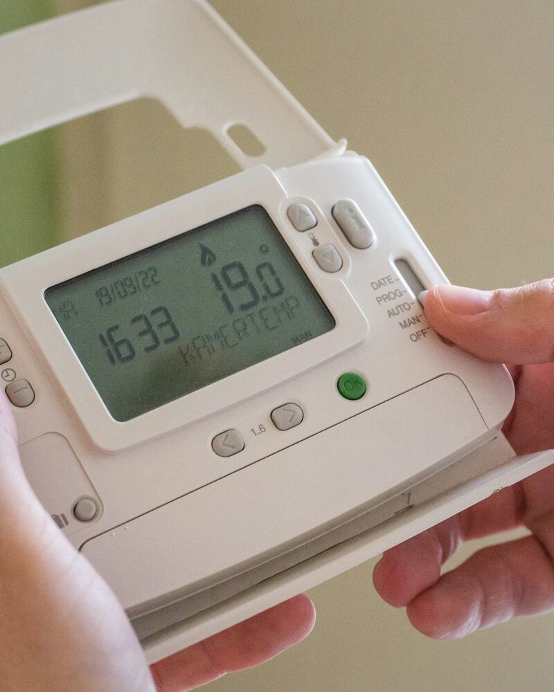 Mains tenant un thermostat programmable affichant 19 degrés.