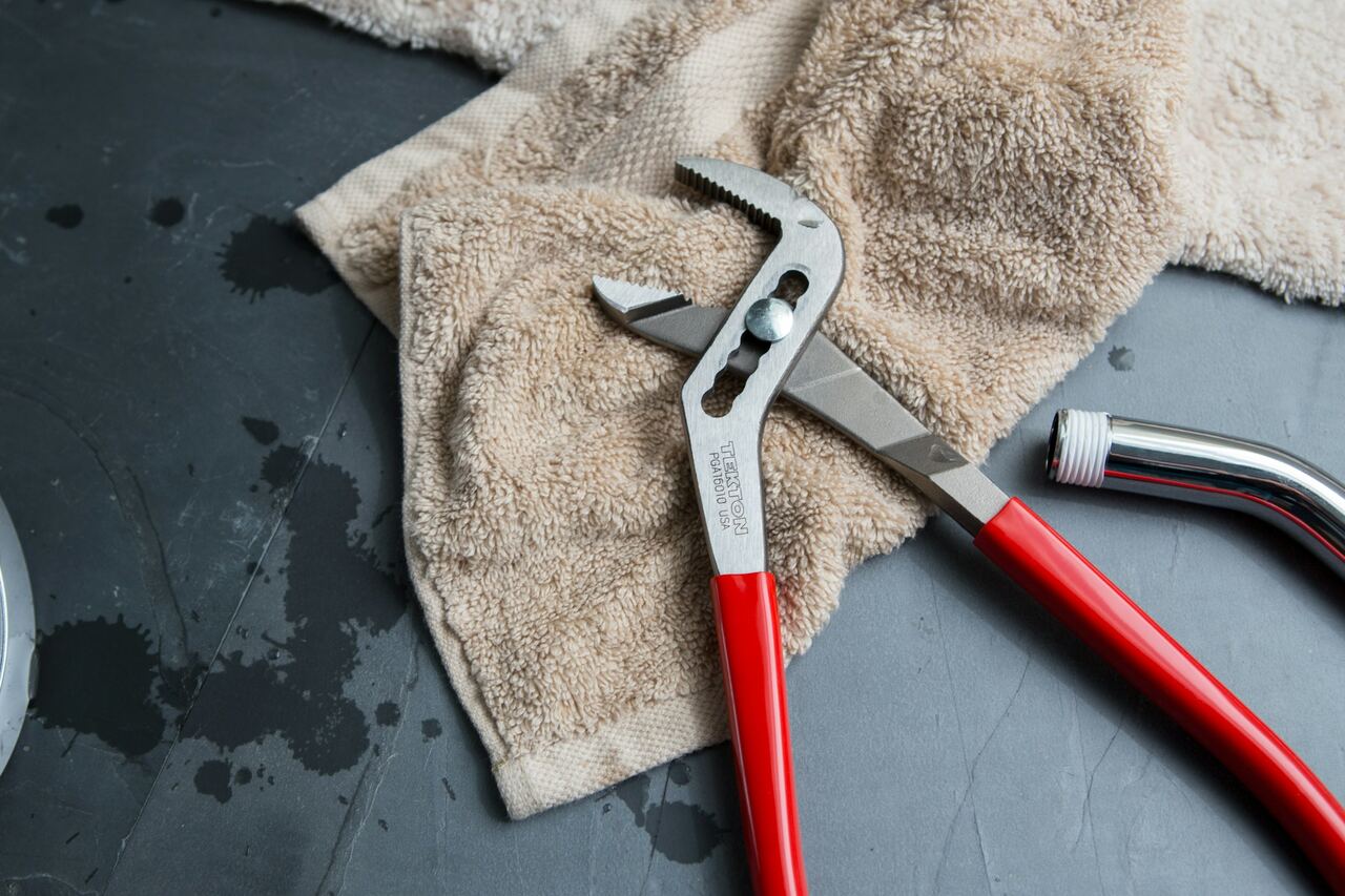 Pince de plombier posée sur une serviette, à côté d’un flexible et d’une pomme de douche.