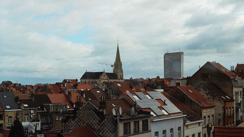Toits de maisons bruxelloises, avec leurs cheminées, un clocher et une tour à l’horizon.
